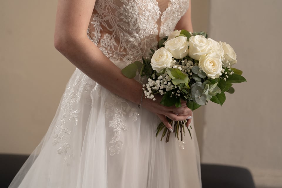 Braut im Spitzenkleid hält einen Brautstrauß aus weißen Rosen
